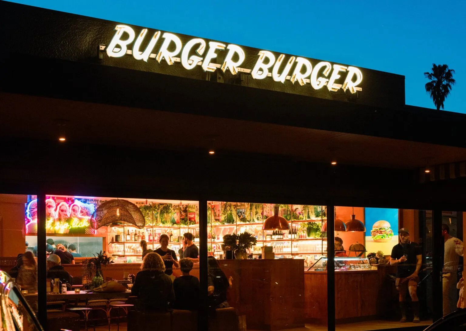 Burger Burger Waiake restaurant at night with lit signage and warm interior lighting
