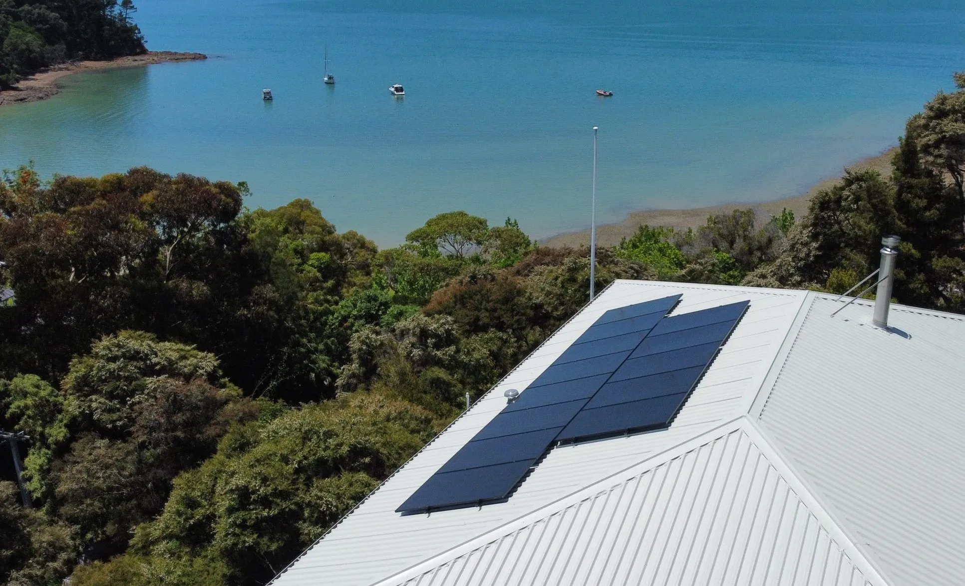 Solar panels on a white metal roof of a coastal Auckland home with the sea behind