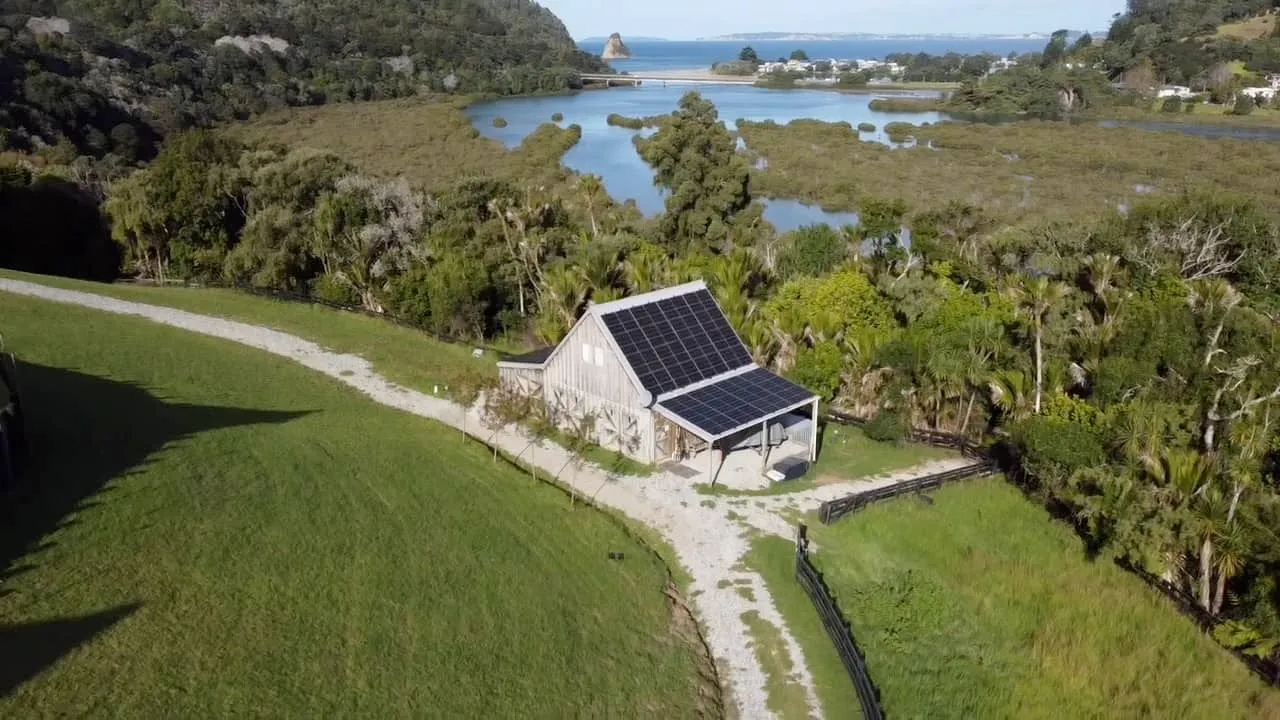 Small barn with solar panels on its roof beside an estuary