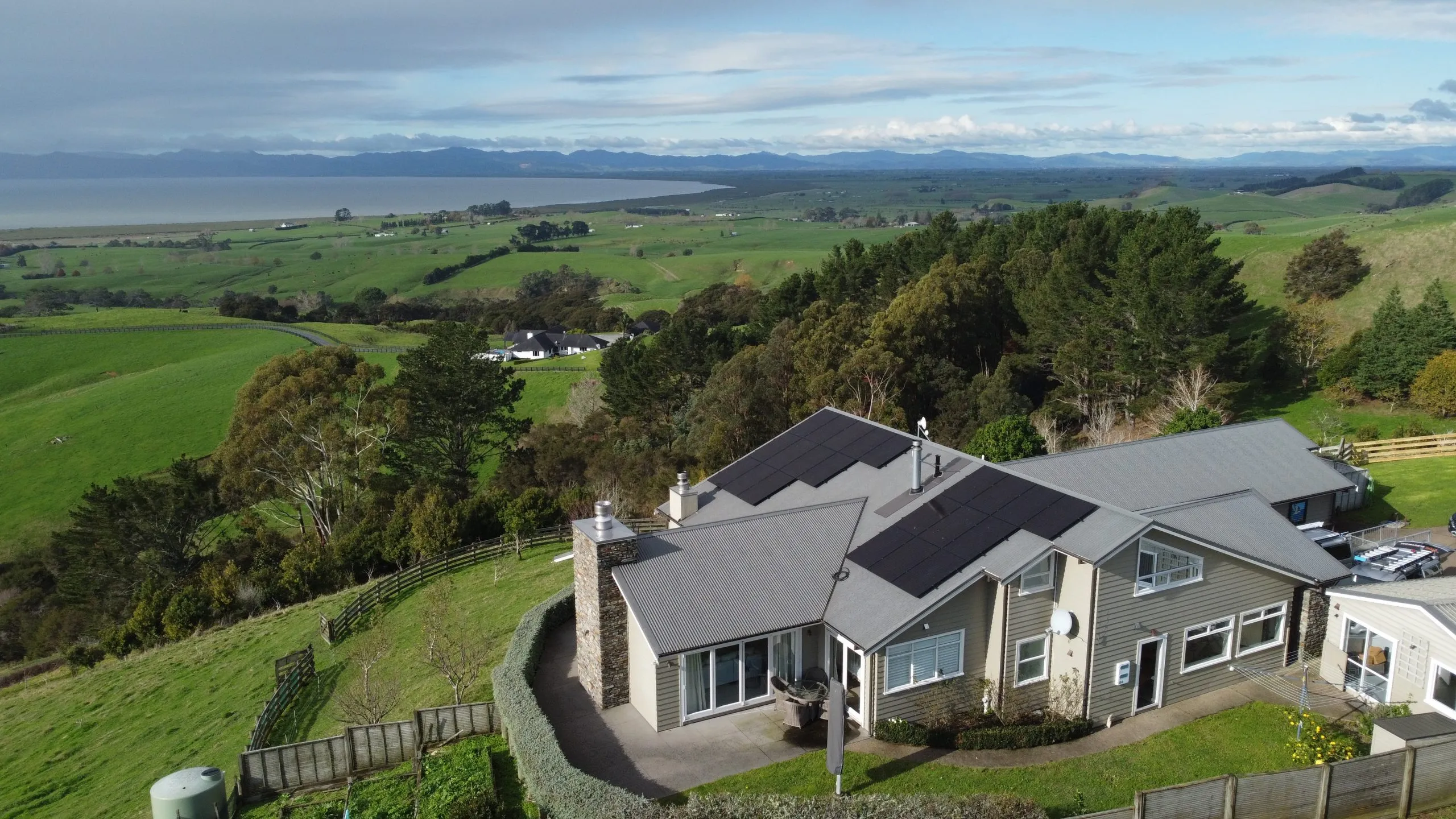 Aerial view of a rural Auckland home with solar panels and farmland behind