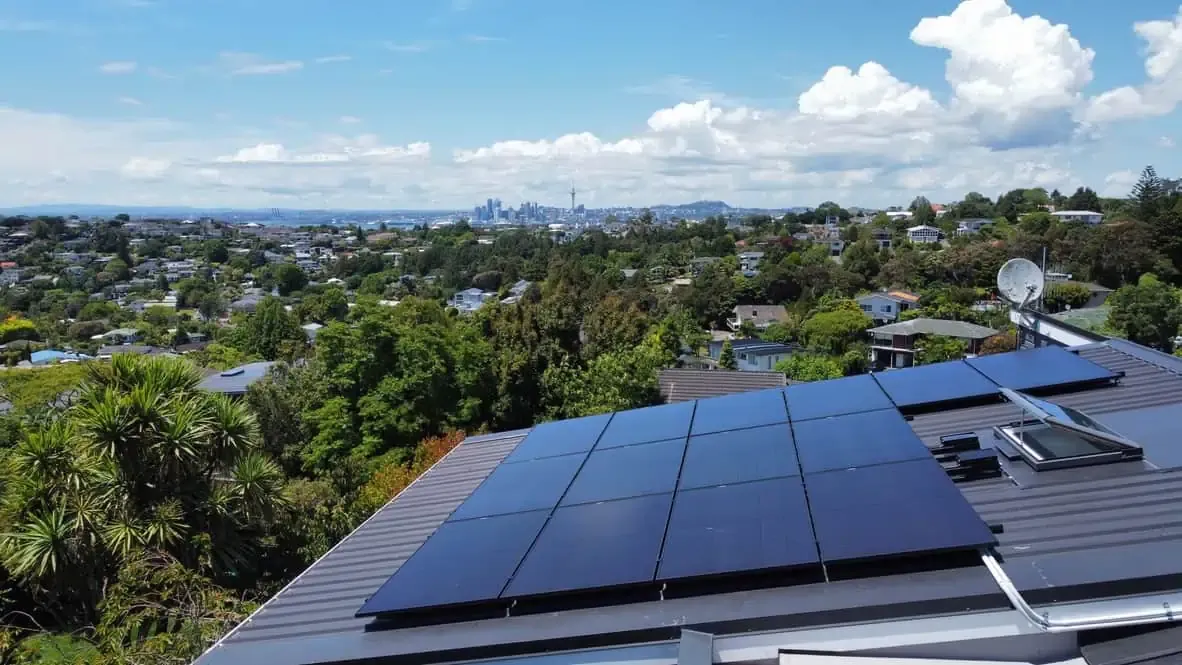 Black solar panels on a roof with the Auckland skyline in the distance
